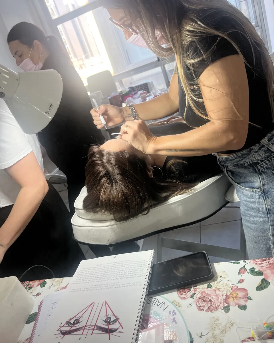 Una profesora trabaja sobre los ojos de una alumna recostada, con el apunte del curso abierto al lado.