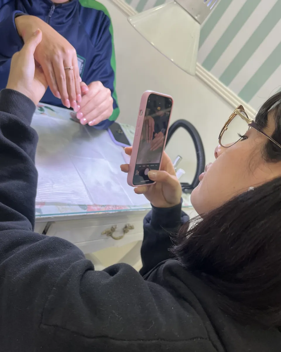 Una alumna fotografía con el celular el trabajo terminado sobre la mano de una compañera.