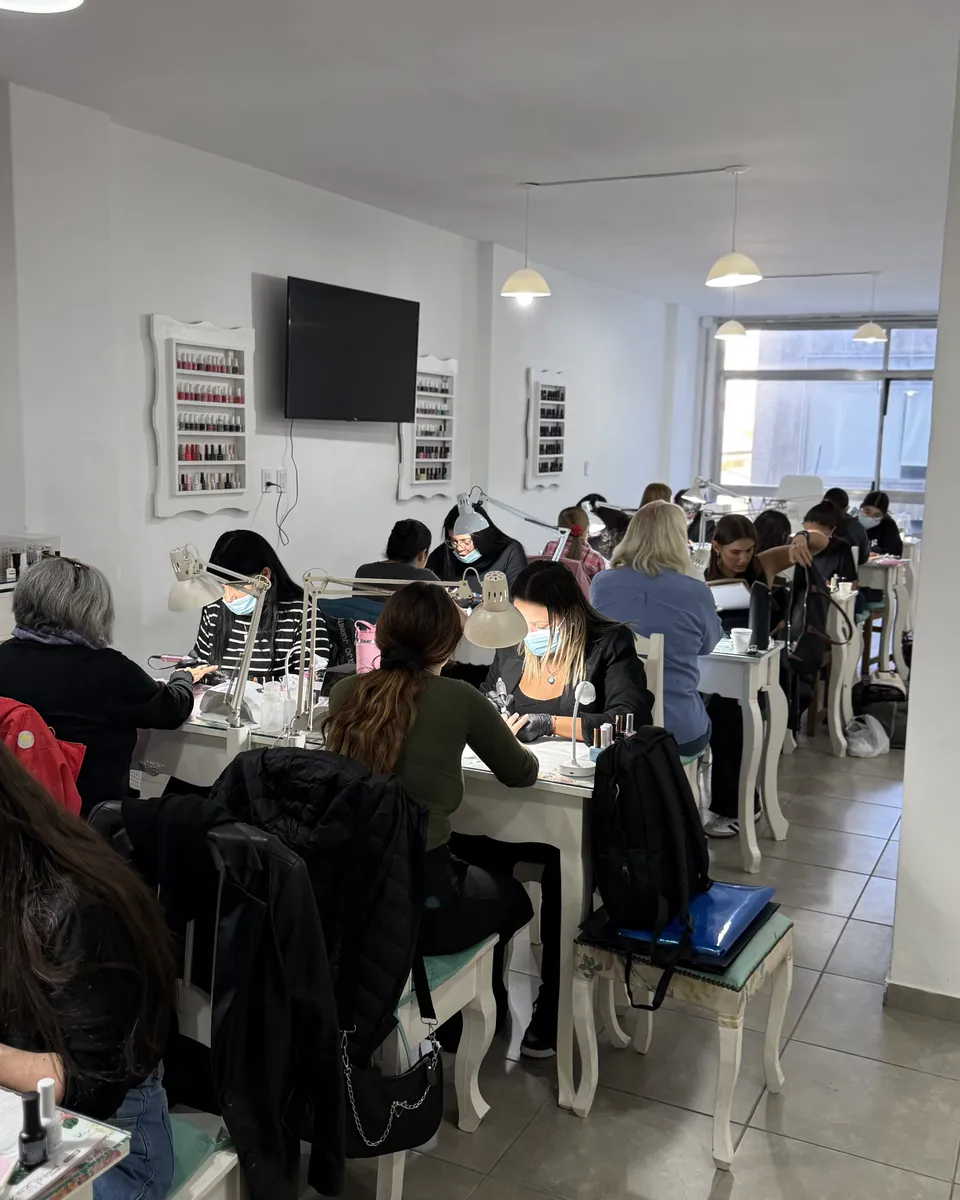 El aula llena: las mesas de manicura ocupadas, cada una con su lámpara, y la pantalla de la clase al fondo.