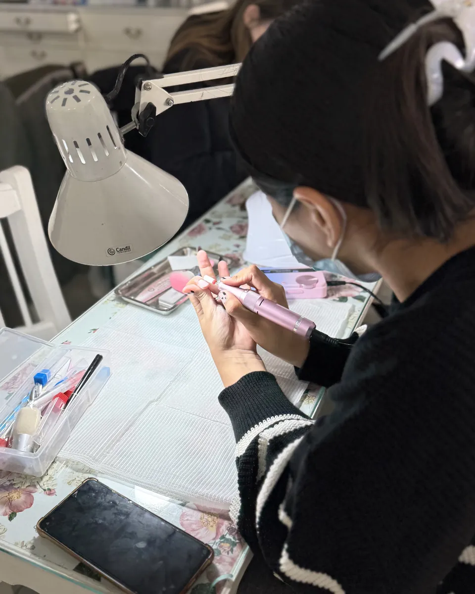 Una alumna con barbijo practicando sobre una mano de entrenamiento, con el torno y los materiales ordenados en la mesa.