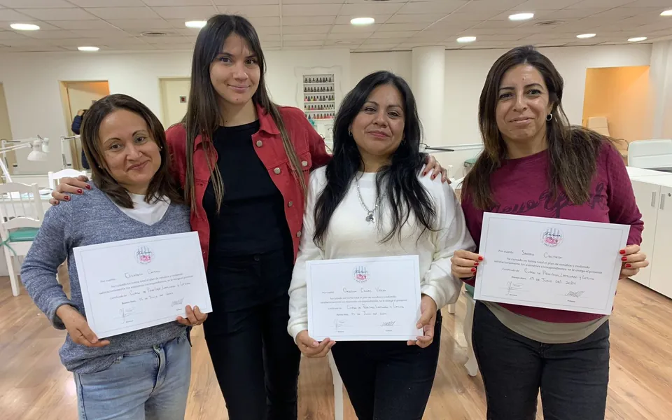 Tres alumnas del curso de perfilado, laminado y lifting con sus certificados, abrazadas con la profesora en el aula.