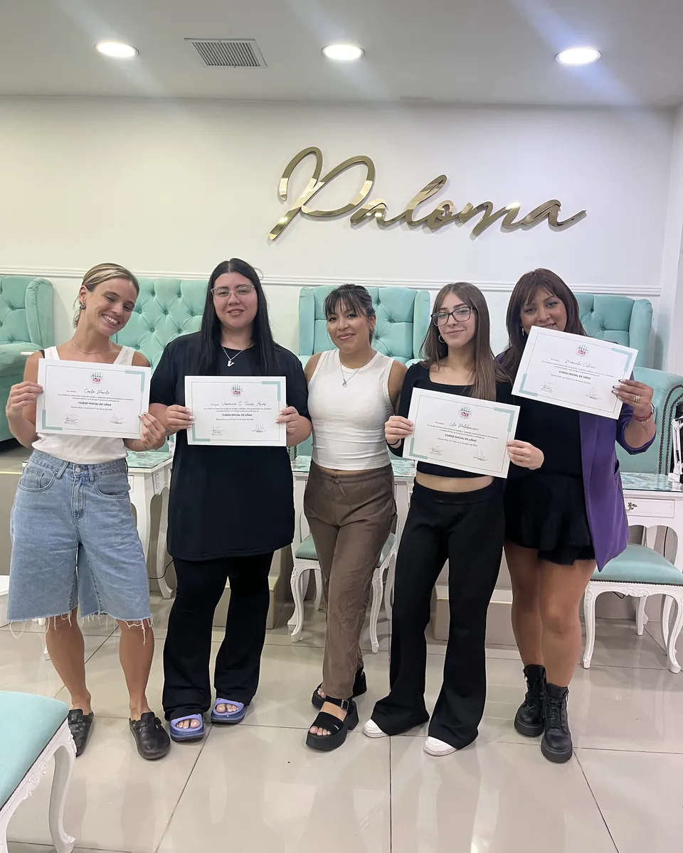 Cinco alumnas sonríen con sus certificados frente a los sillones turquesa y el logo dorado de Paloma.